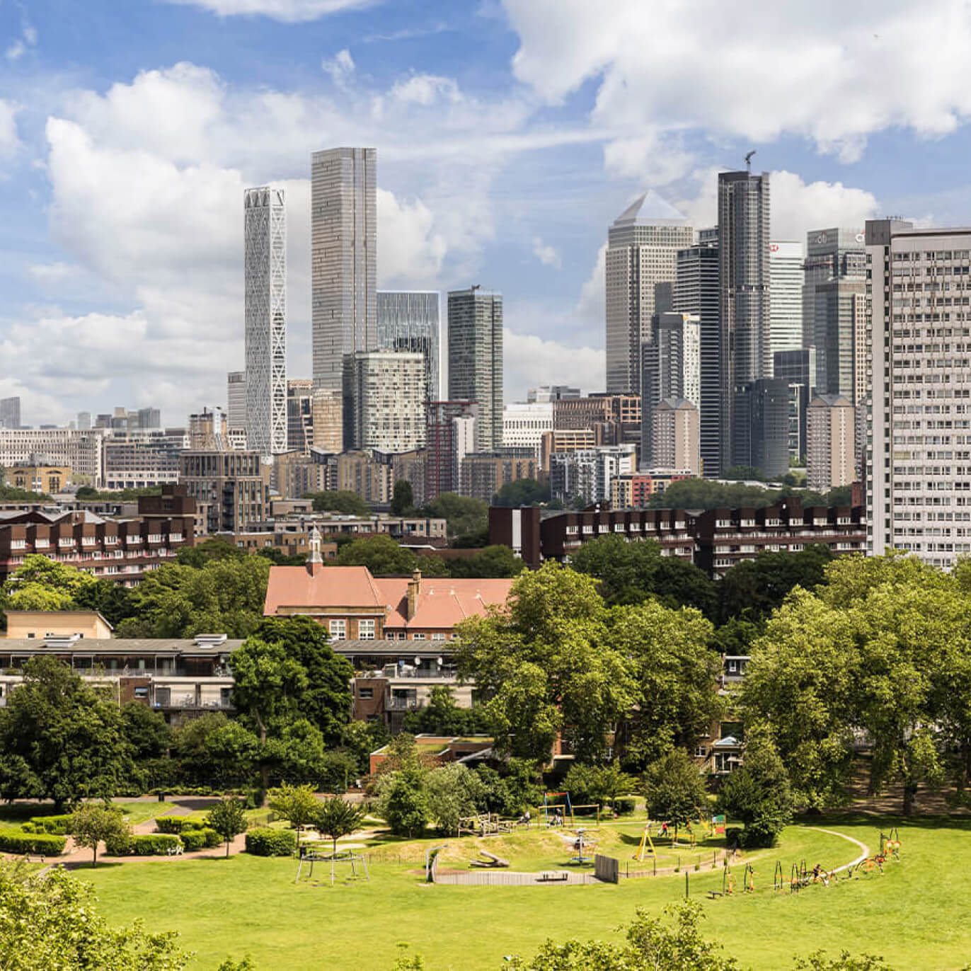 A cityscape showing a modern skyline with tall glass skyscrapers, mid-rise buildings, and a lush green park featuring playground equipment, trees, and hints of golf activities.