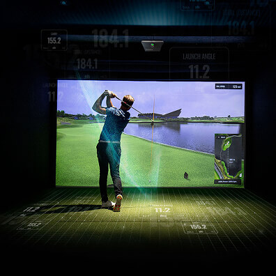 A person swings a golf club in an indoor golf simulator, facing a large screen displaying a realistic golf course scene with stats and metrics—perfect for those seeking golf memberships or practicing year-round in Golf London.