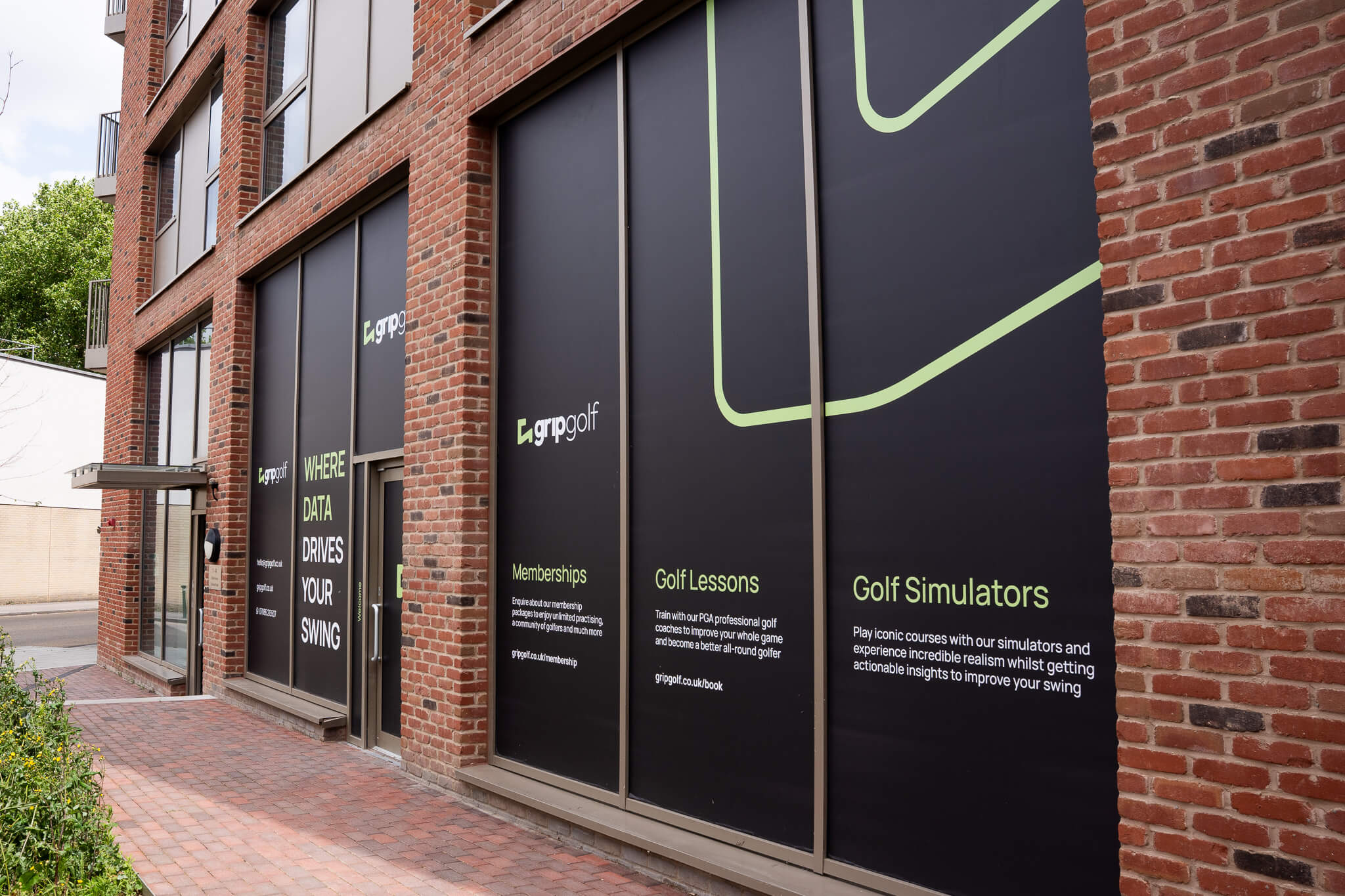 A brick building with large black window panels displaying advertisements for golf london, featuring text about golf memberships, golf lessons, and simulators, along with green and white graphics.