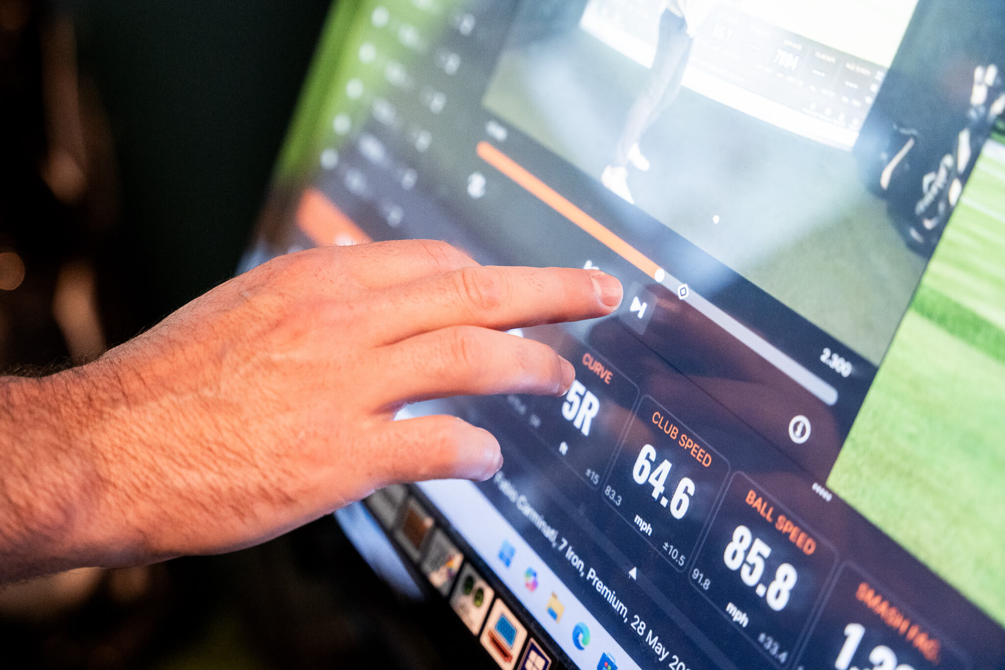 A person’s hand touches a digital screen displaying golf swing data, including club speed, curve, and ball speed—ideal for improving your game with personalized golf lessons or exploring exclusive golf memberships.